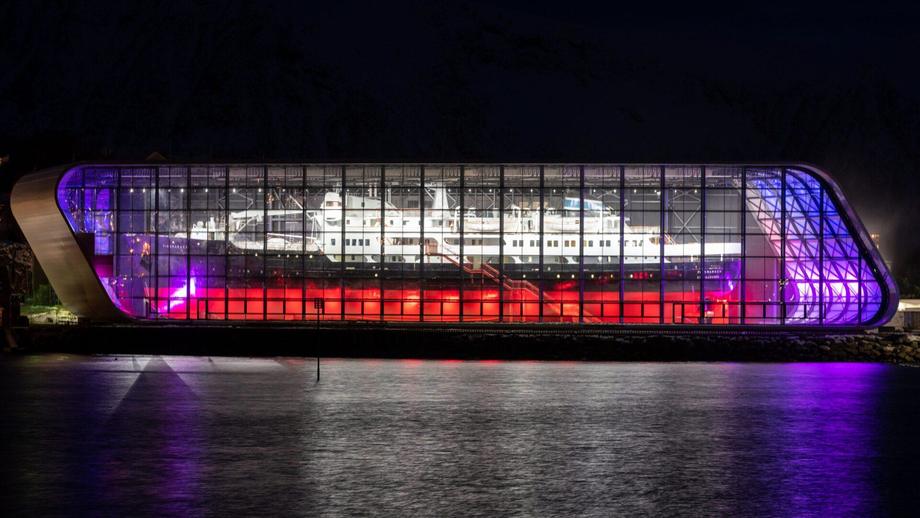 Flott kveldsbilde av hurtigrutemuseet i Stokmarknes opplyst innvendig med nybygg rundt hurtigruten.